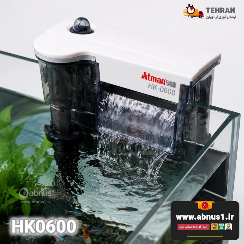فیلترهای آویزان آتمن، مدل HK-0600 است. در نمای روی جعبه، دستگاهی با ابعاد بزرگ و بدنه کریستالی شفاف دیده می‌شود که نشان‌دهنده حجم بالای مخزن مدیا برای فیلتراسیون حرفه‌ای است. در این تصویر، خروجی آبشاری عریض دستگاه که جریانی قدرتمند اما آرام را به نمایش می‌گذارد، به همراه لوله مکش مجهز به اسکیمر (چربی‌گیر) سطح آب به وضوح مشخص است. همچنین نشان “Super Fit” روی بسته‌بندی، گویای طراحی مهندسی شده برای نصب پایدار بر روی لبه آکواریوم‌های بزرگ با ضخامت شیشه‌های مختلف می‌باشد. بدنه شفاف به کاربر اجازه می‌دهد تا بدون باز کردن درب، وضعیت پاکیزگی فیلتر را رصد کند.